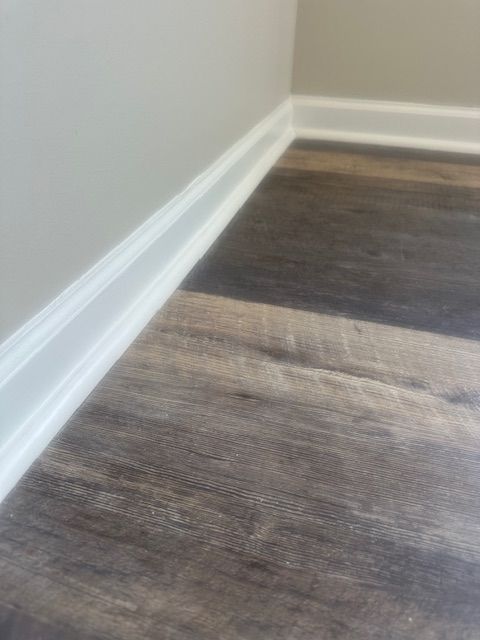 Dark wood-look floor with white trim along a light gray wall.