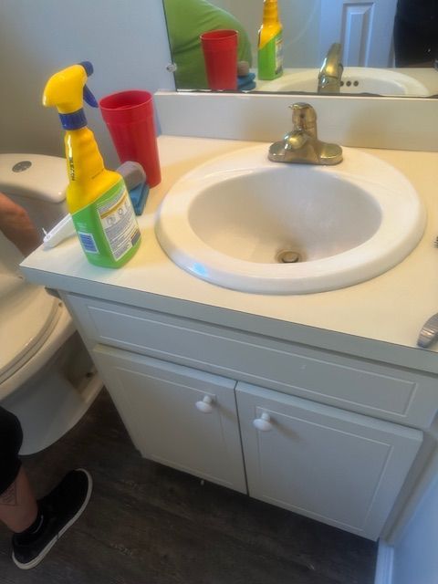 Bathroom vanity with sink, cleaning spray, red cup. White cabinets, beige countertop.
