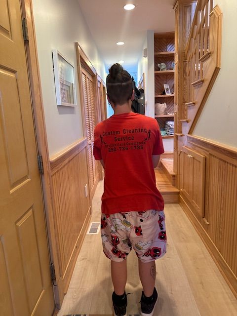 Person in red t-shirt and patterned shorts walking down hallway with wood paneling and stairs.