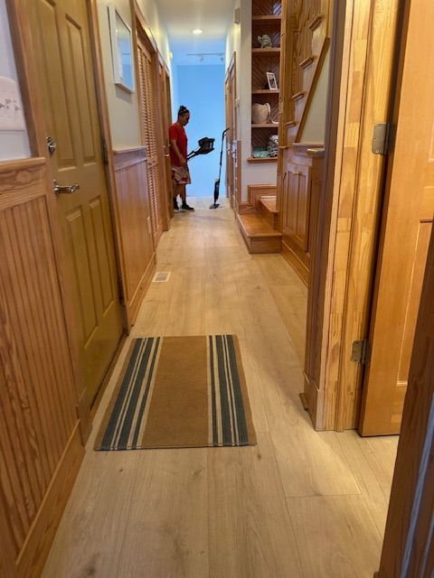 A person vacuums a hallway with wood paneling, floor, and stairs.