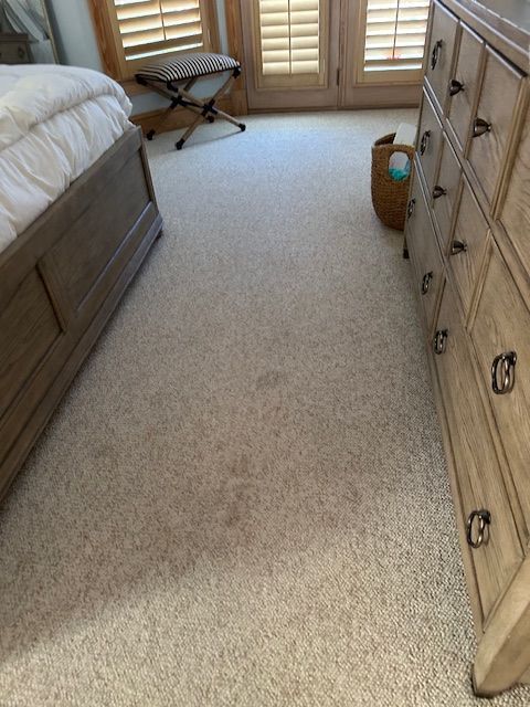 Beige carpet in a bedroom with a bed on the left, dresser on the right, and windows with shutters.