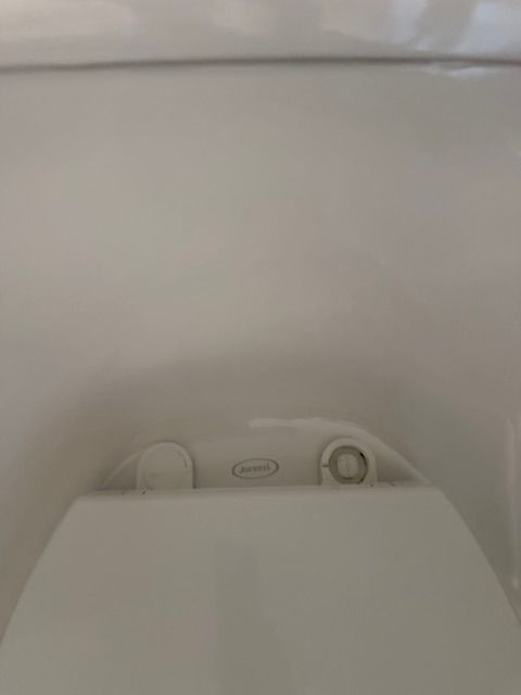 Top-down view of a white toilet seat with a central control panel and a small dial on the right.