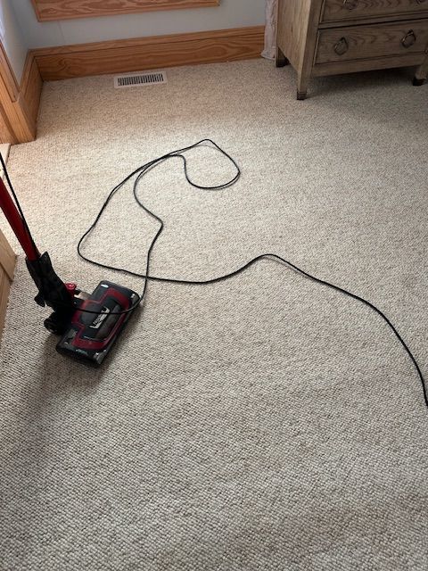 Vacuum cleaner on beige carpet in a room; cord sprawled out.