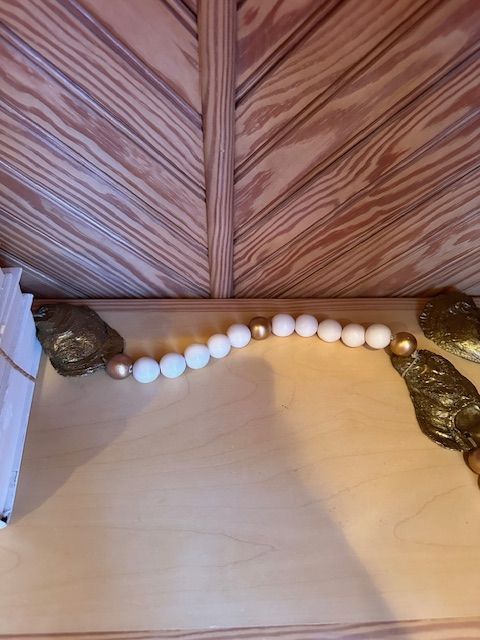 Wooden beaded garland with gold accents hangs above a wooden shelf.