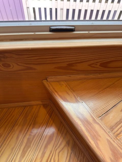 Wooden staircase with a shiny, varnished finish, leading up to a window.