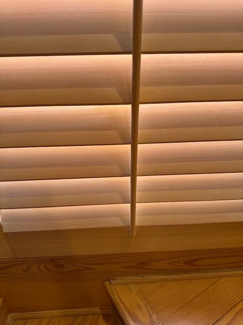 Wooden blinds with a central control rod, angled downwards. Soft natural light.