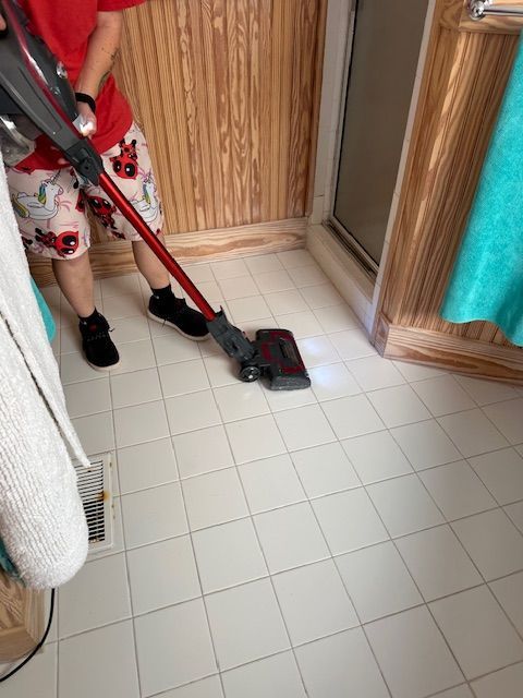 Person vacuuming a white tile bathroom floor with a red and black vacuum cleaner.