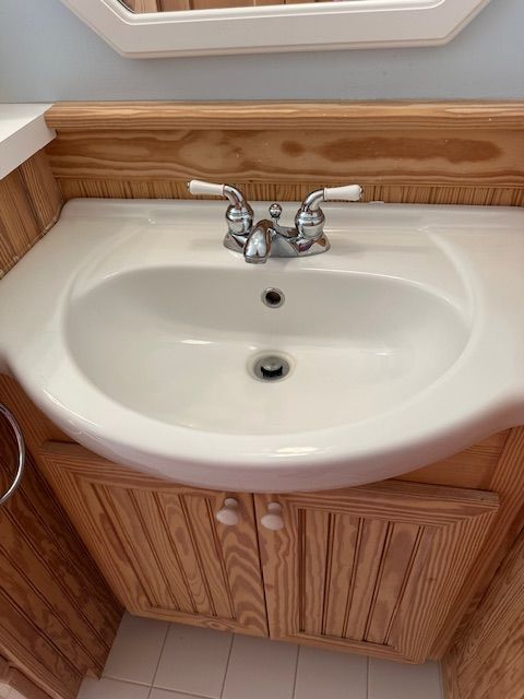 White bathroom sink with chrome faucet and wooden cabinet, set against a light-colored wall.