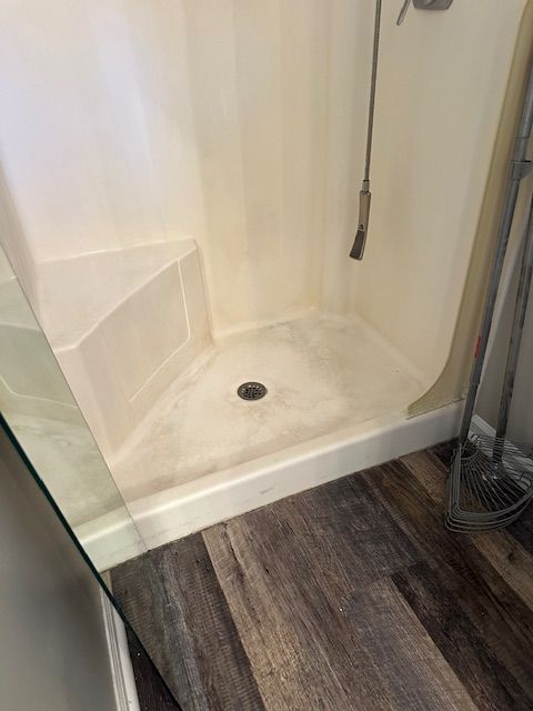 Tiled, triangular shower with a built-in seat. The floor is wood-look laminate, and there's a glass shower door on one side.