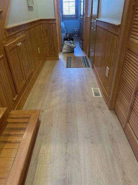 Hallway with wood paneling, light wood floor, leading to a room with a window.