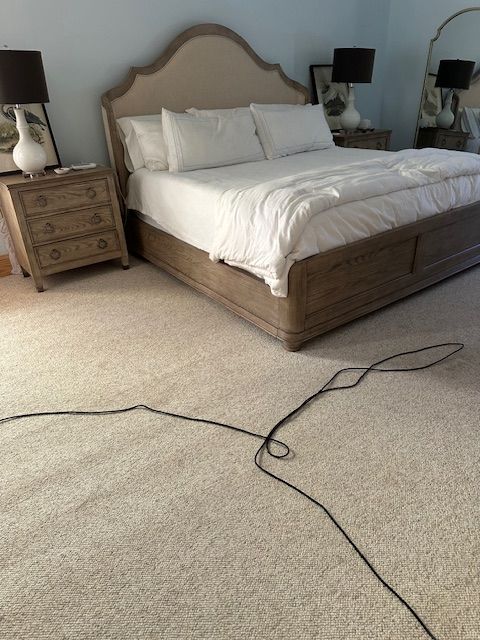Bedroom with bed, nightstands, lamps, and a tangled black cord on the light-colored carpet.