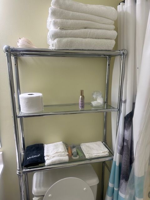 Chrome shelving unit with white towels, toilet paper, and toiletries in a bathroom.