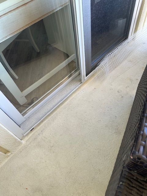 Sliding glass door, tan patio. Wire mesh along the bottom edge. Dark wicker chair on right side.