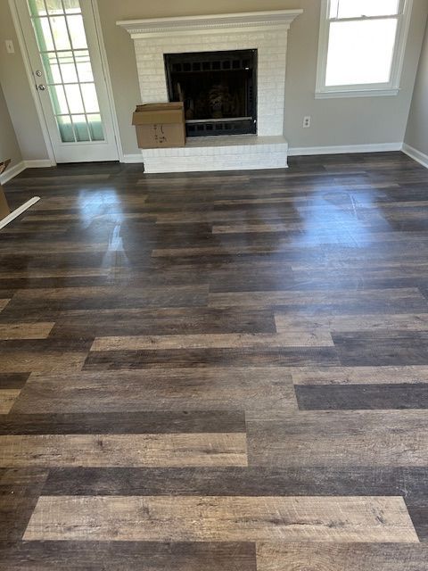 Wooden plank flooring in a room with a white fireplace and door, natural lighting.