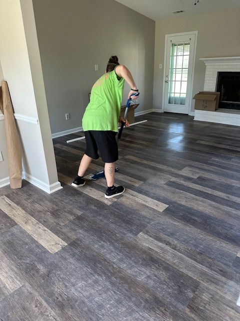 Person mopping a new wood-look floor in a living room with a fireplace and white trim.