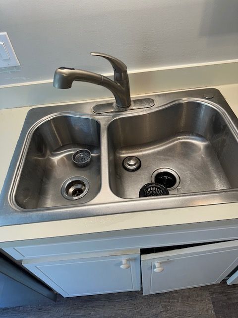 Stainless steel kitchen sink with two basins and a faucet. A cabinet door is ajar.