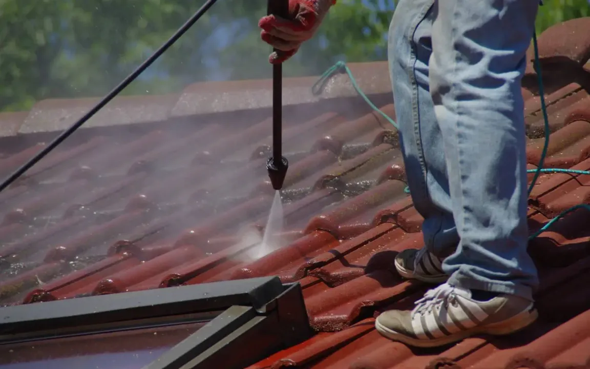 A man is cleaning a tiled roof with a high pressure washer.