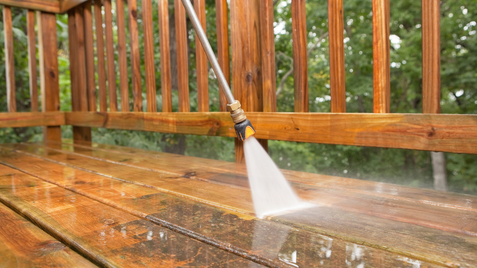 A person is using a high pressure washer to clean a wooden deck.