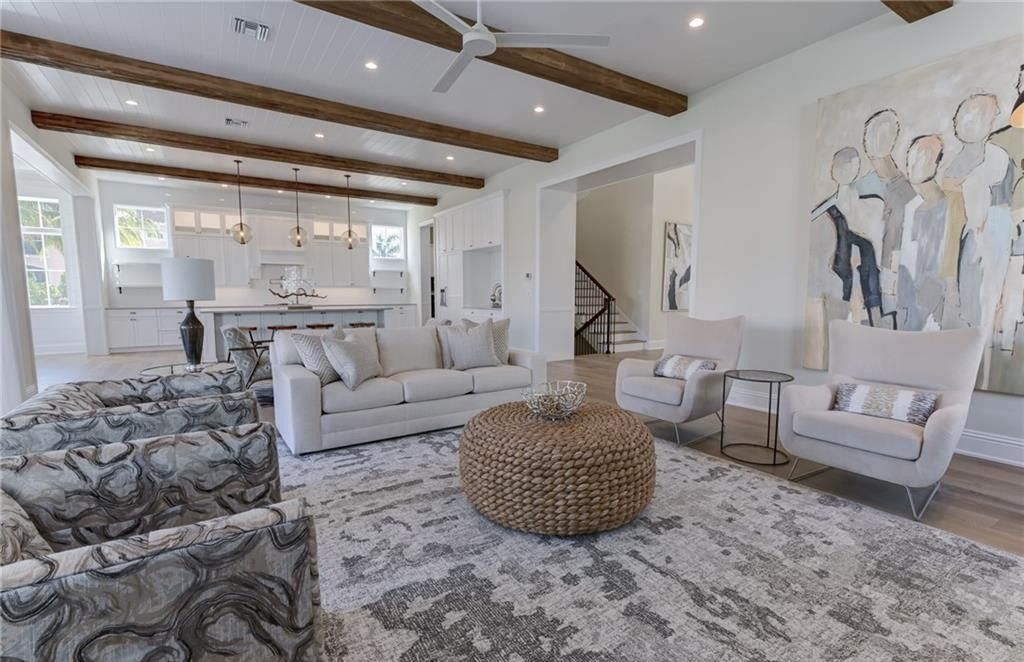 Living room with light-colored furnishings, area rug, and wooden beams. Open to a kitchen.