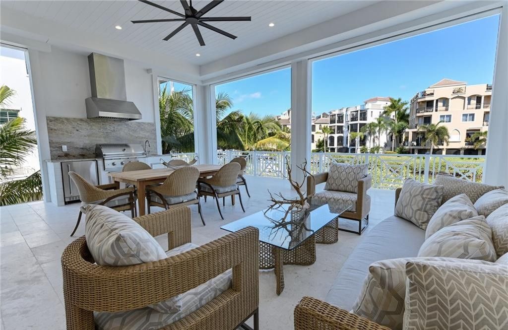 Covered outdoor patio with seating, dining, and a built-in kitchen, overlooking a waterway.