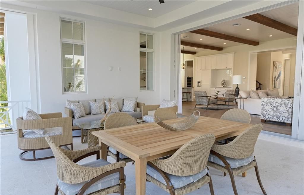 Outdoor patio with wooden dining table and chairs, sofa, opening to a bright interior.