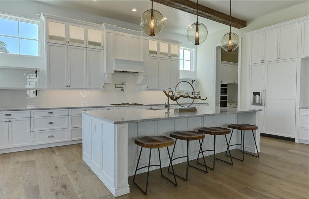 White kitchen with island, wooden stools, and pendant lights.