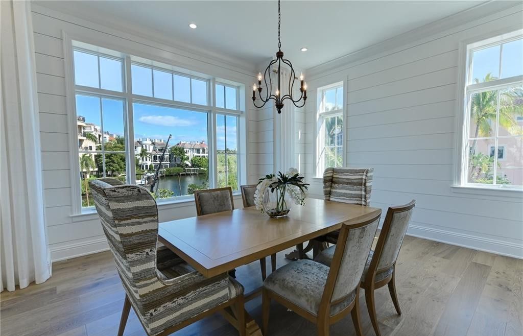 Dining room with wooden table, patterned chairs, large windows, and chandelier.
