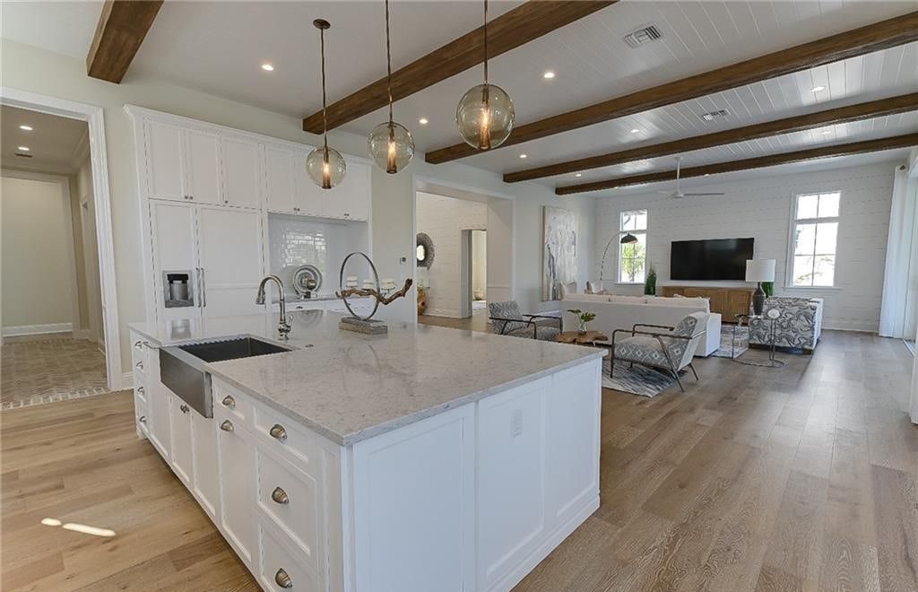Open-concept kitchen and living area with white cabinets, wood beams, and hardwood floors.