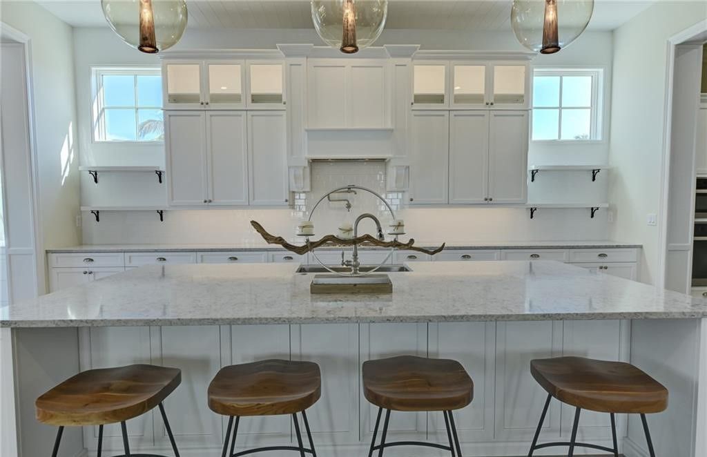 White kitchen with island, wooden stools, cabinets, and hanging lights.