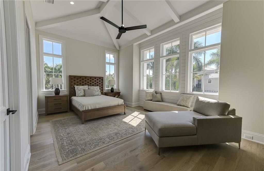 Spacious bedroom with bed, sofa, and windows. Light walls, wood floors, and neutral tones.