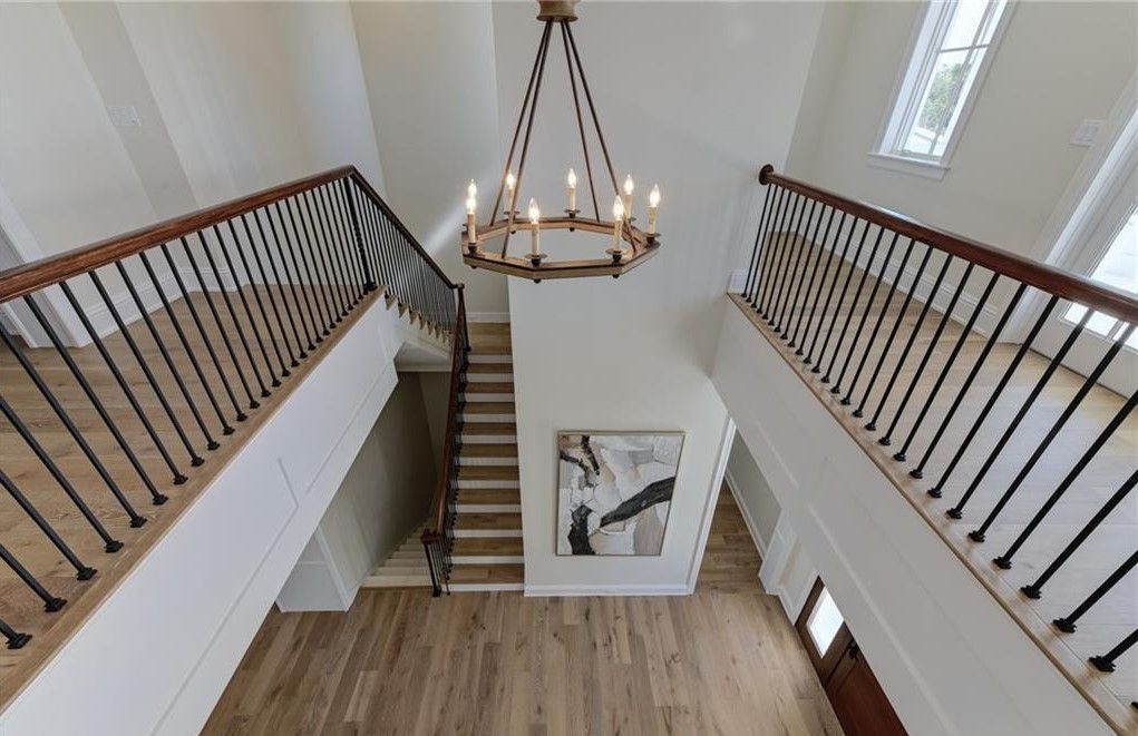 High-angle view of a two-story foyer with dual staircases, wooden floors, and a chandelier.