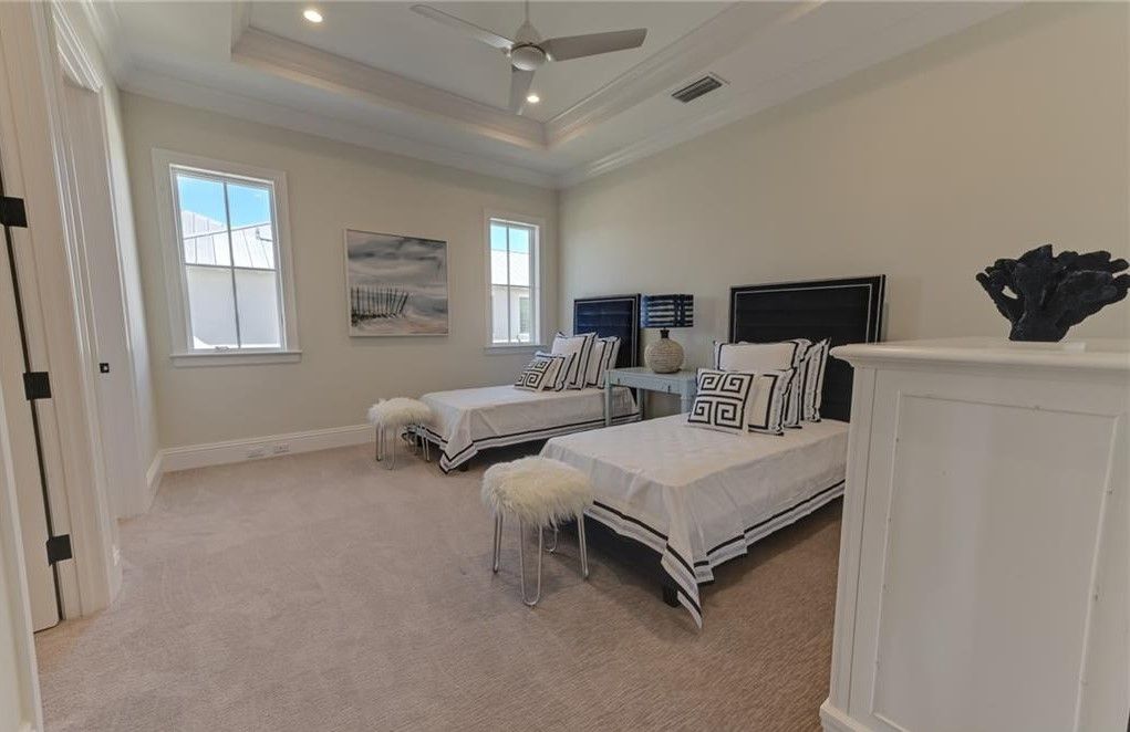 Spacious bedroom with two twin beds, white walls, and light-colored carpet; two windows and a ceiling fan.