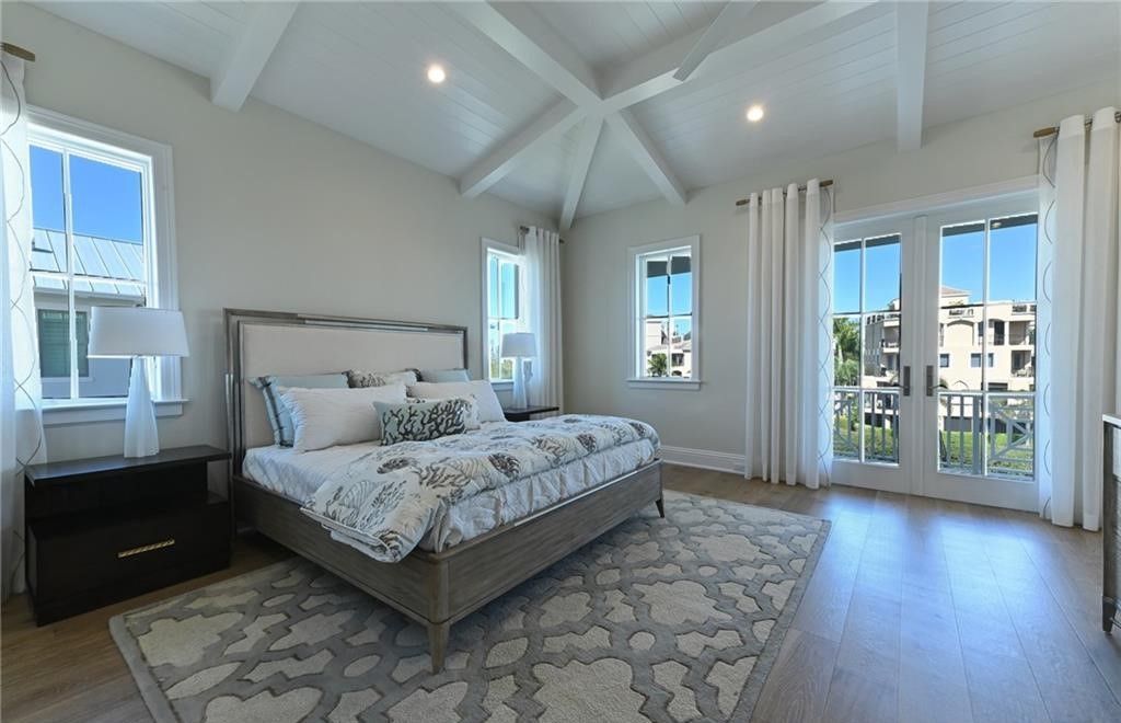 Bedroom with a king bed, patterned rug, white walls, and French doors leading outside.