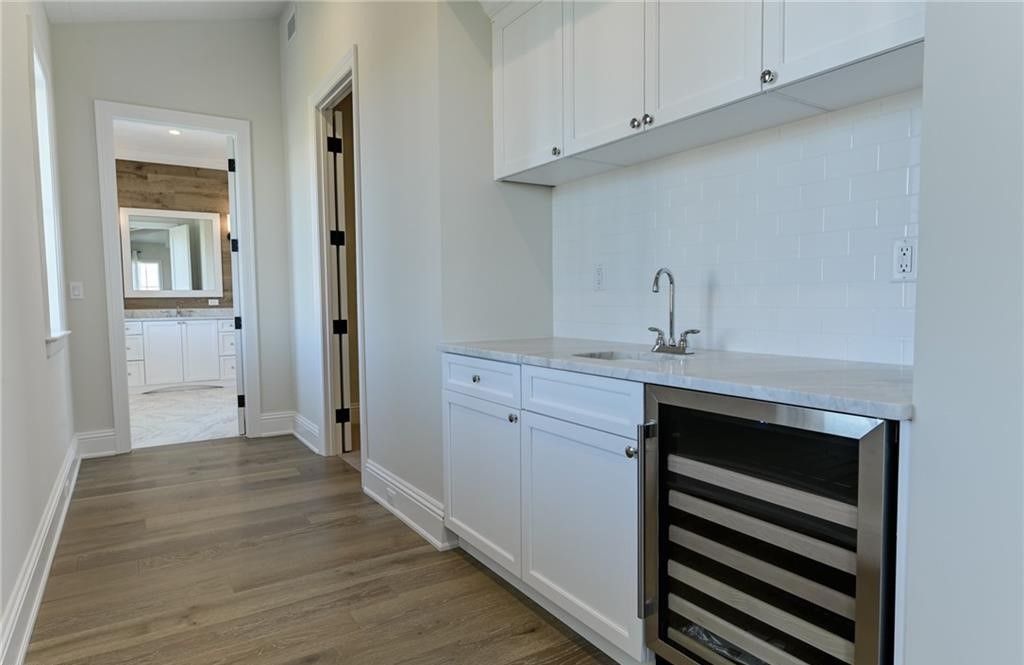 Hallway with white cabinets, a sink, a mini-fridge, and a doorway to a bathroom.