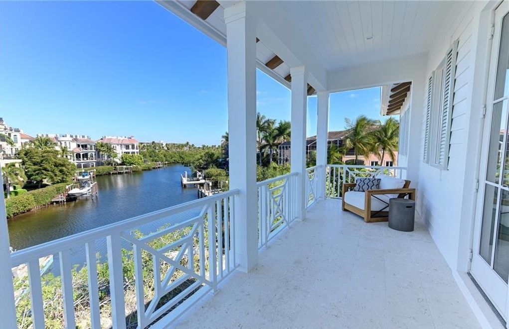 White balcony overlooking a waterway with boats, houses, and trees on a sunny day.