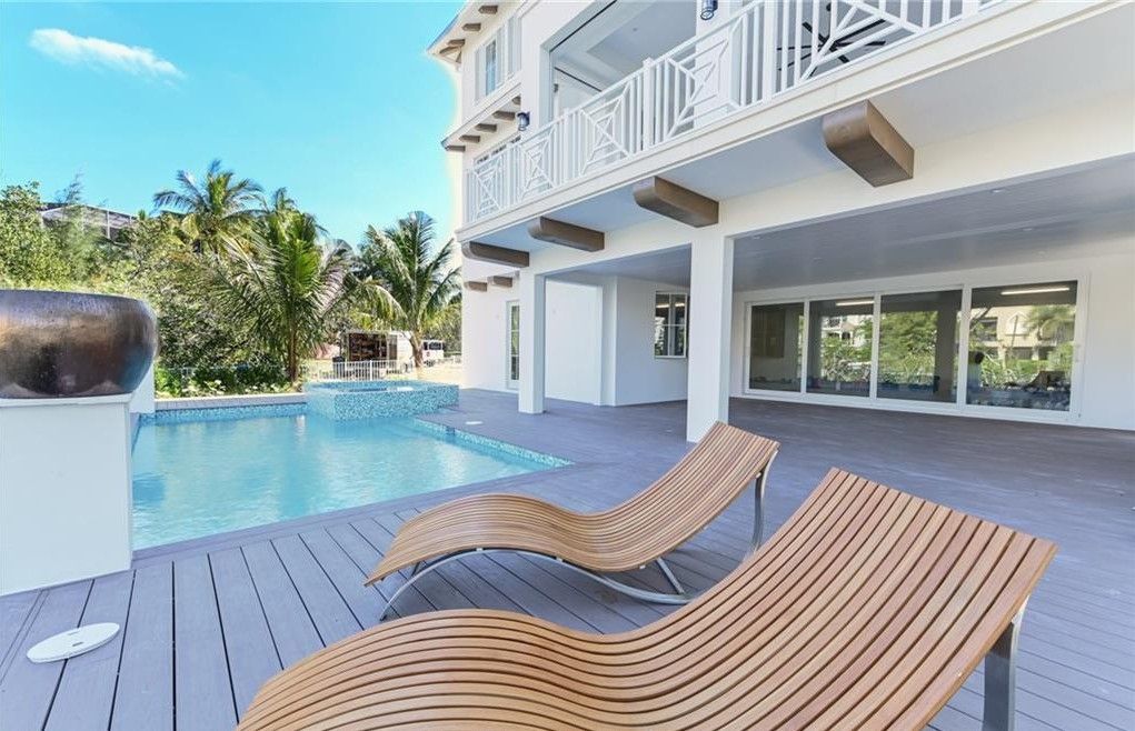 Poolside lounge chairs next to a pool and white house with balcony.
