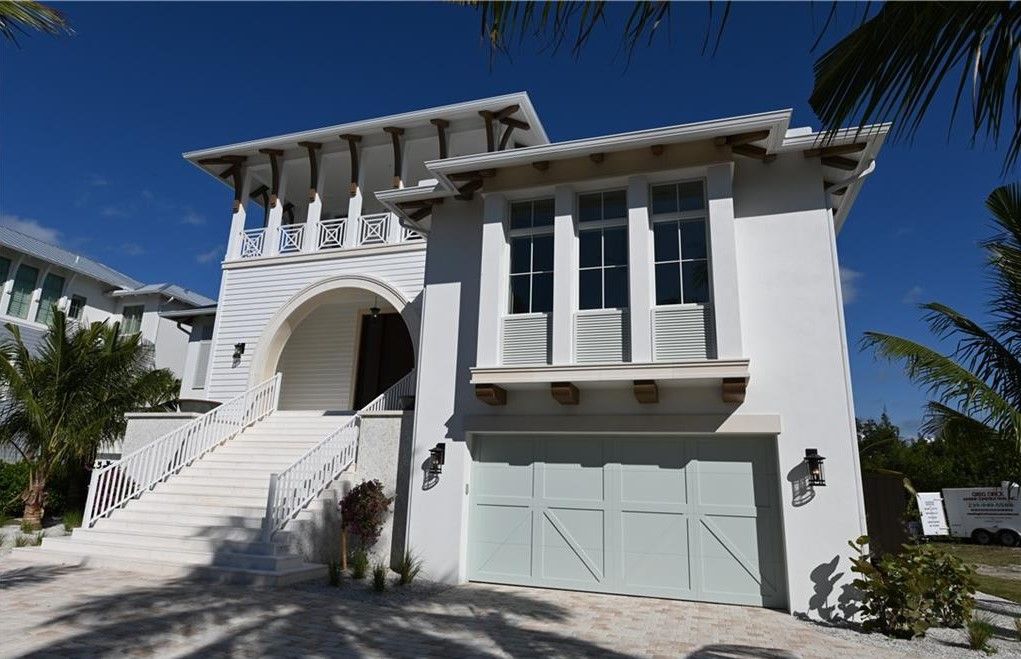White stucco house with arched entrance, stairs, and garage under a blue sky.