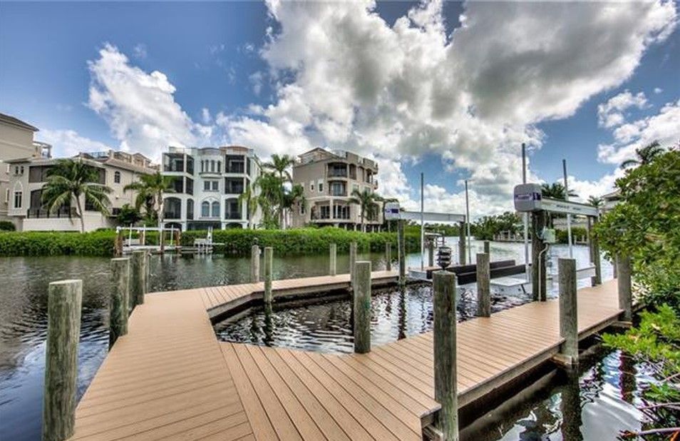 Dock with boats, luxury homes, and blue sky with clouds.