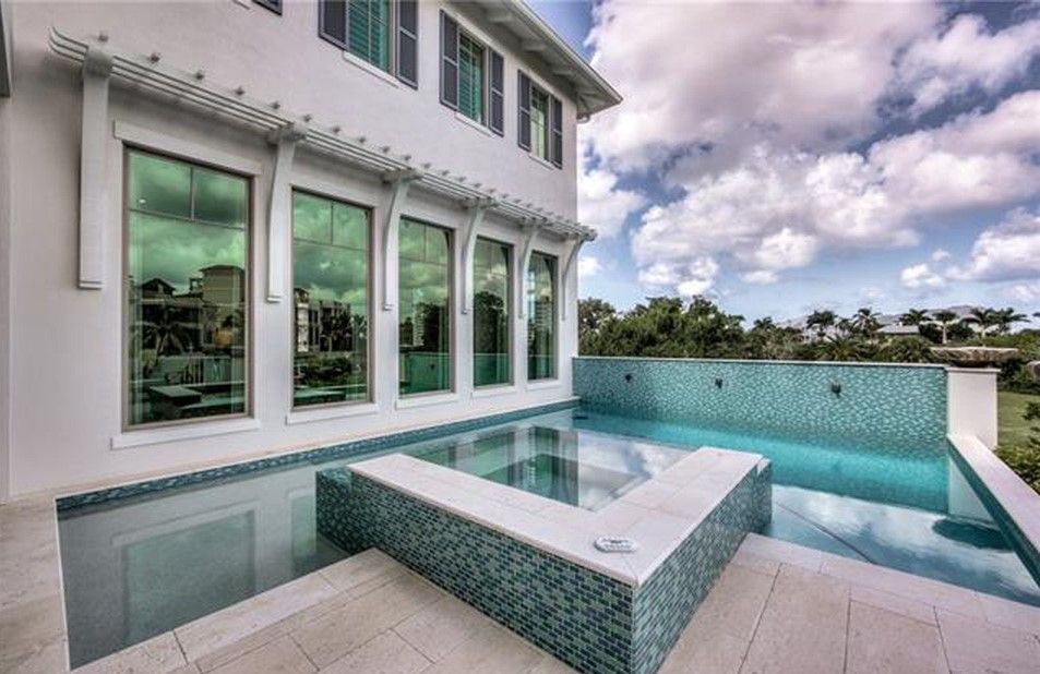 White house with a pool and tile surround. Turquoise water reflects the sky, green-tinted windows.
