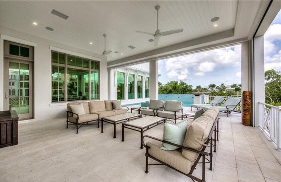 Covered patio with outdoor furniture overlooking a pool and trees. Bright, airy space with neutral colors.