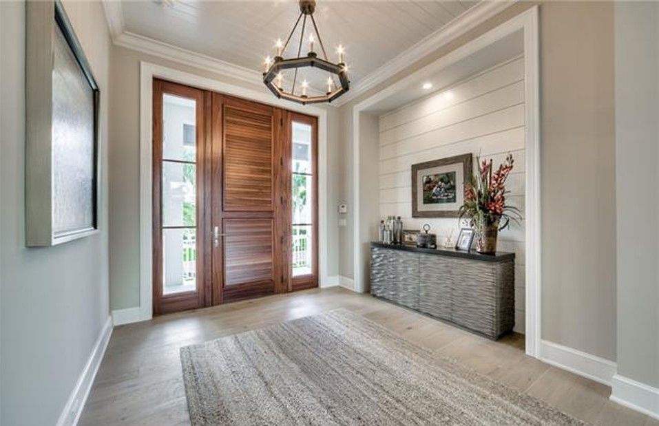 Entryway with wooden door, rug, and console table with artwork. Soft gray walls and chandelier.