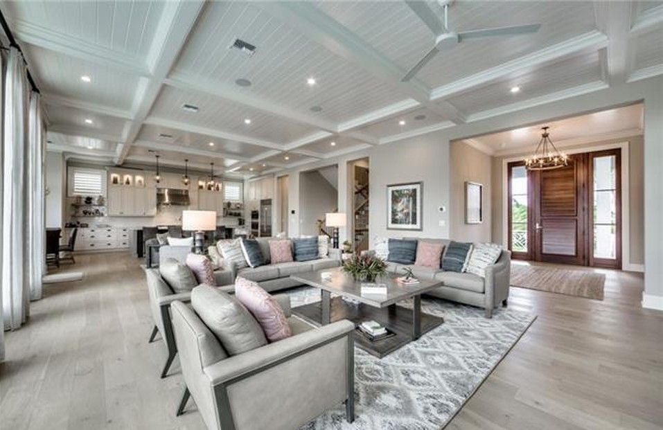 Spacious living room with gray furniture, rug, and coffered ceiling, open to kitchen and entrance.