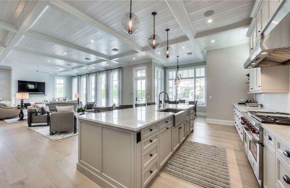Spacious, bright kitchen with a large island, connected to a living area. White cabinets, light wood floors, and pendant lights.