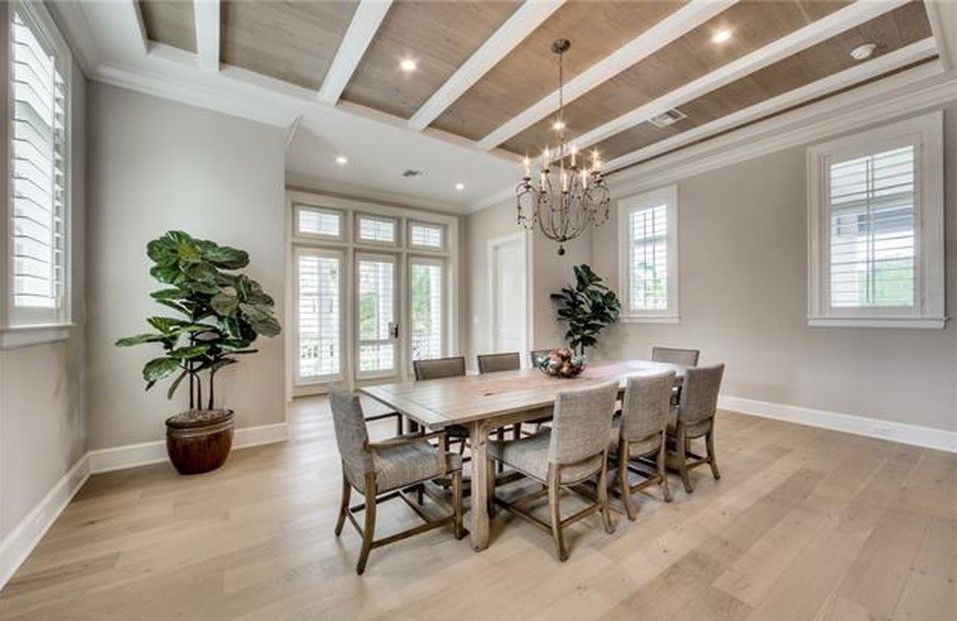 Dining room with light wood floors, a long table with chairs, chandelier, and large windows.