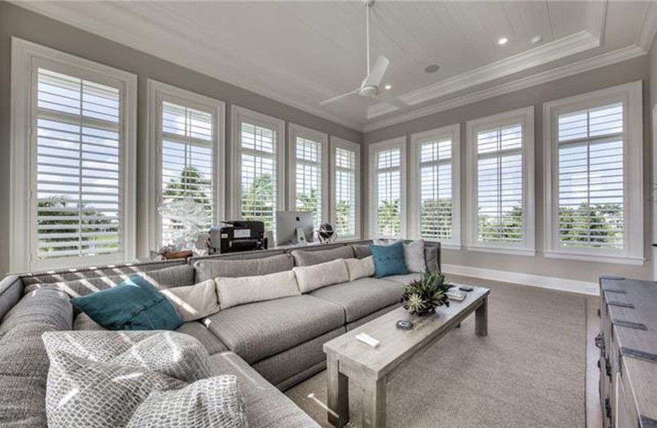 Living room with large gray sectional sofa, multiple windows with white shutters, and a coffee table.