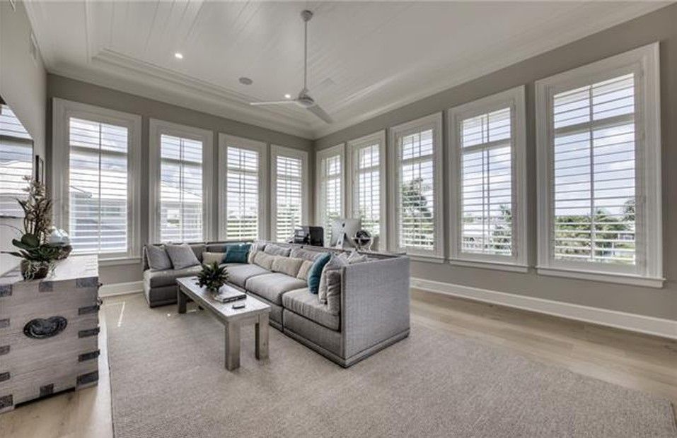 Living room with gray sectional sofa, tall windows, white shutters, and a light-colored rug.