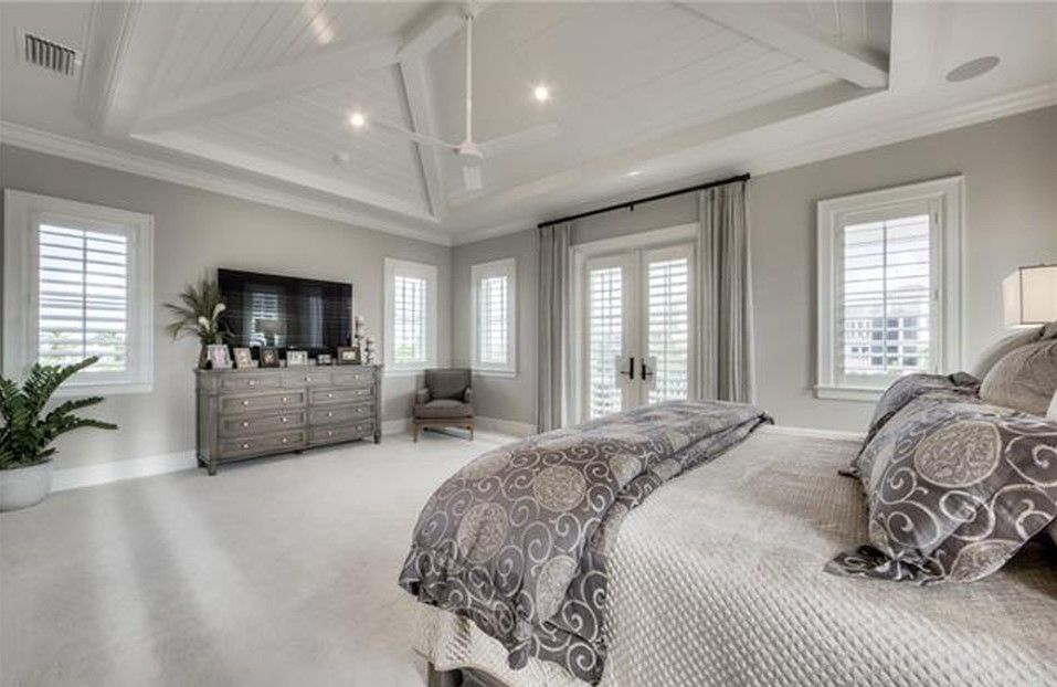 Spacious bedroom with a large bed, TV, and French doors leading to a balcony. Neutral color palette.