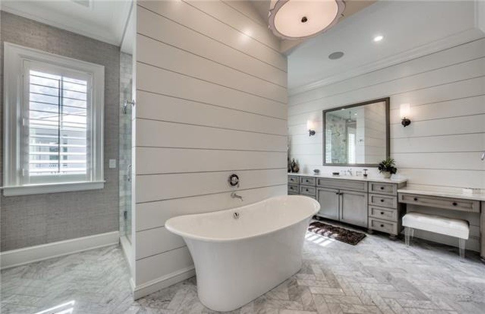White claw-foot tub in a bright bathroom with gray shiplap walls and a vanity.
