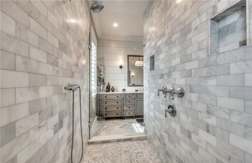 Luxurious marble-tiled walk-in shower leads to vanity. Silver fixtures, recessed shelving.
