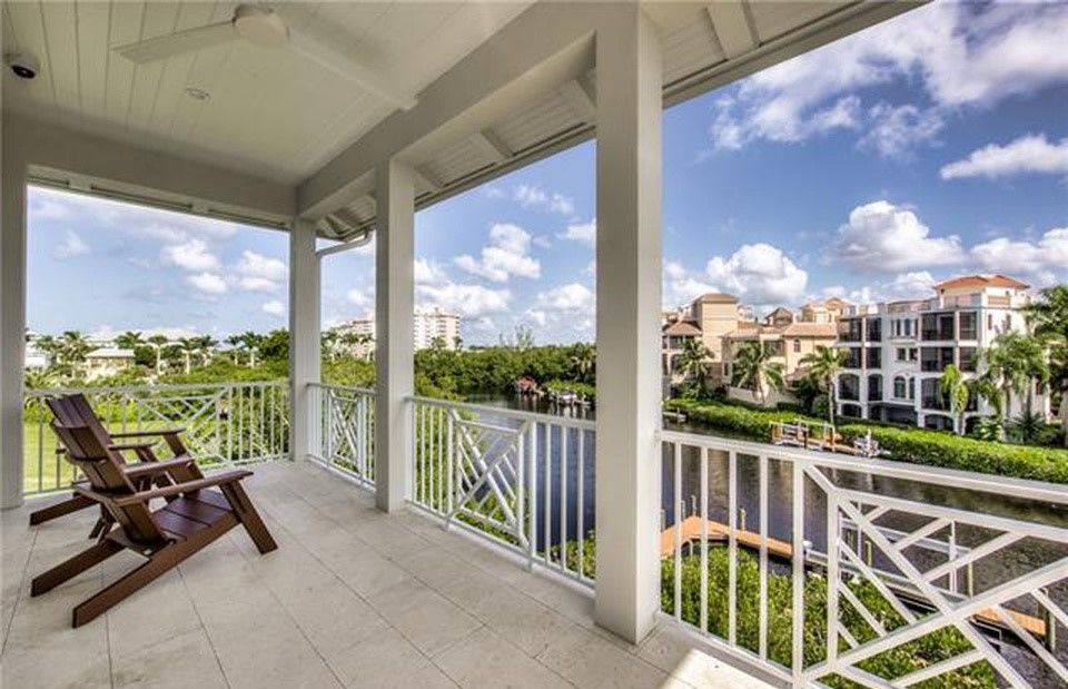 Balcony overlooking a canal with two wooden chairs, white railing, and buildings.